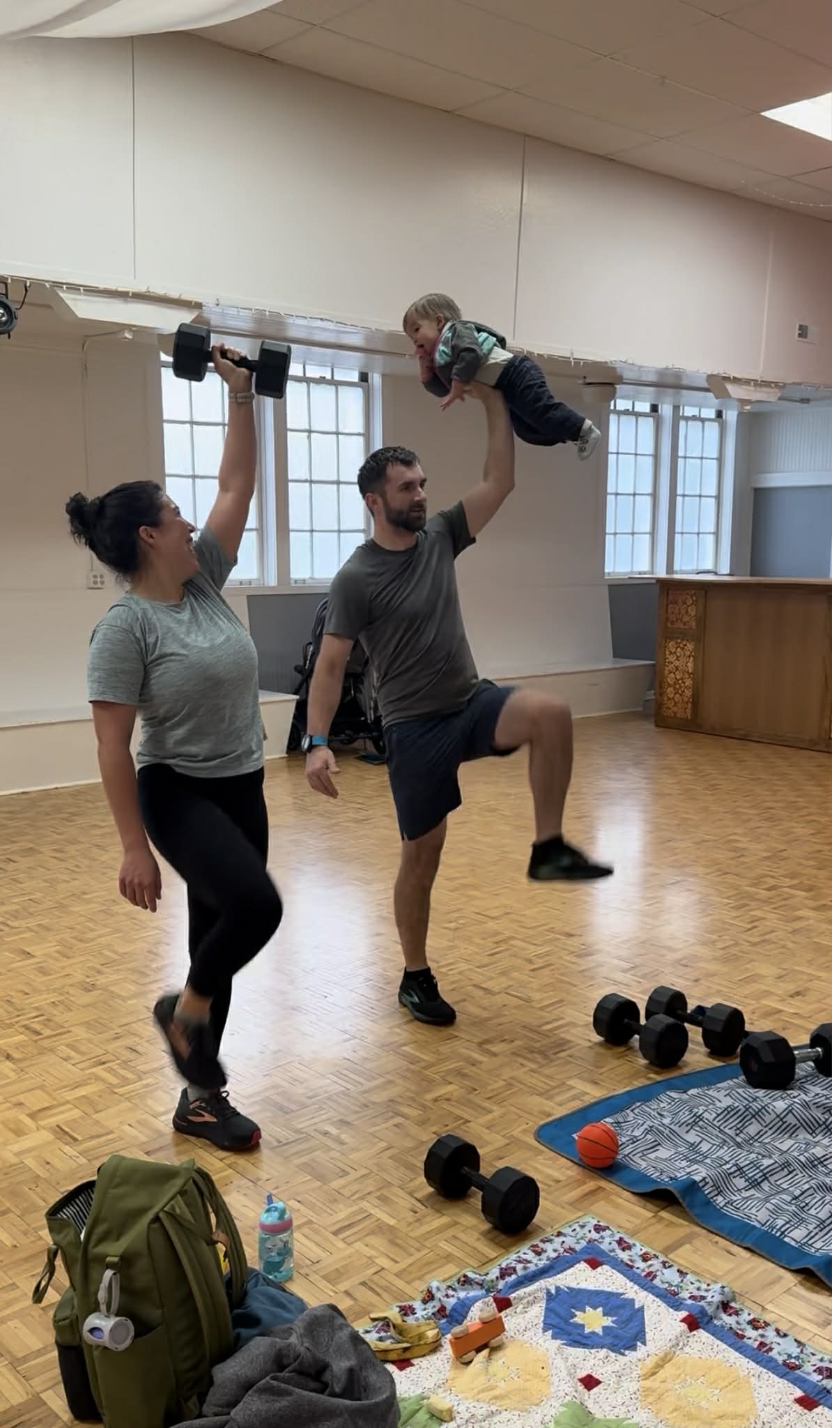 Dad lifting child overhead while mom works out with dumbbells