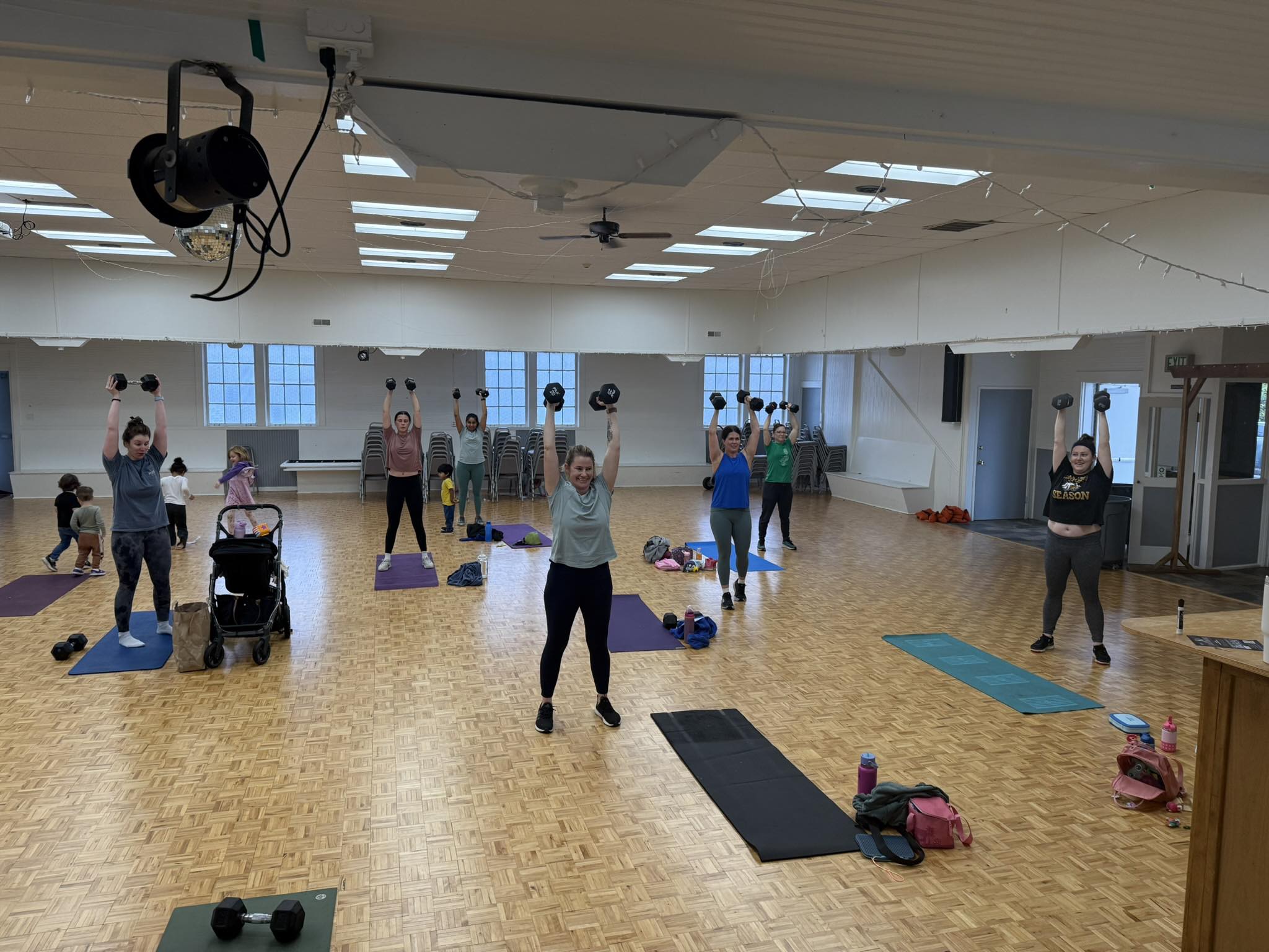 Class members pressing dumbbells overhead during workout