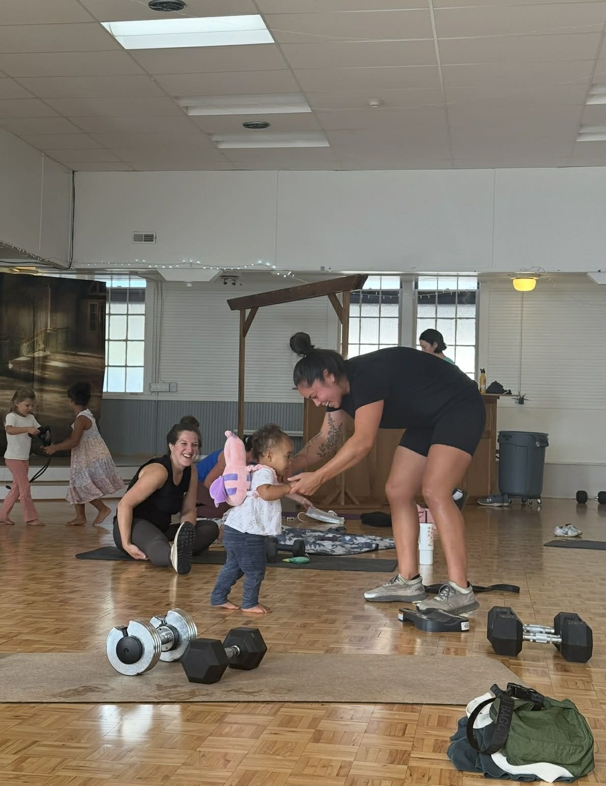 Mom pausing workout to interact with toddler while other members smile