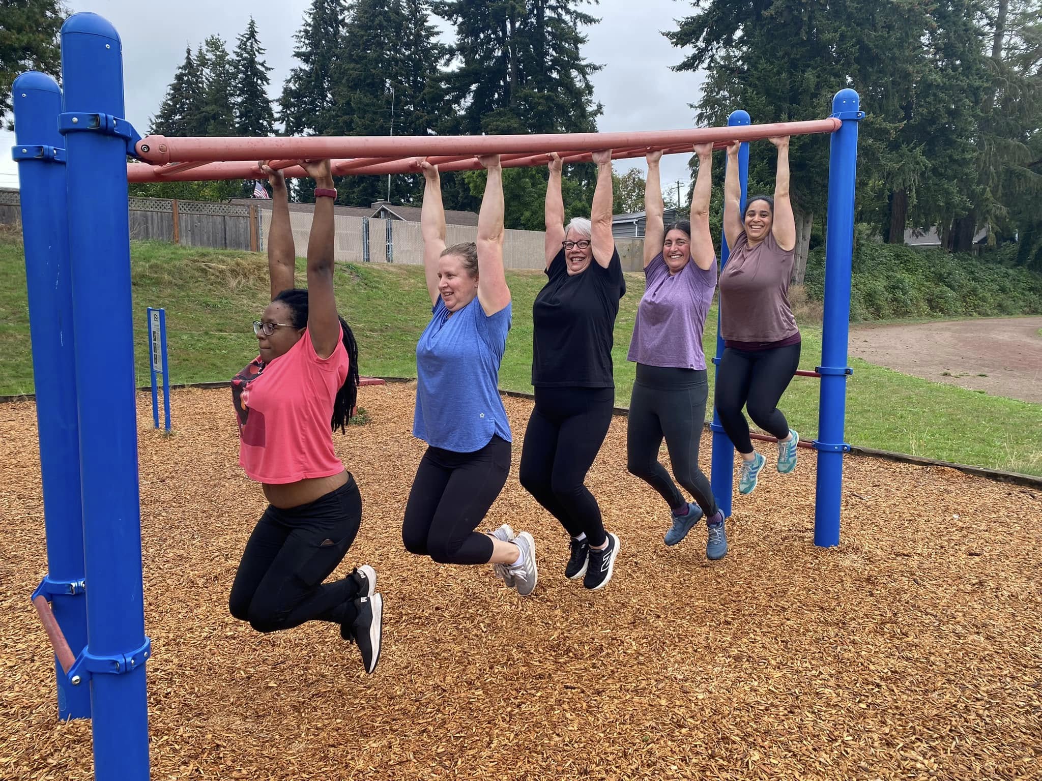 Member hanging from monkey bars at outdoor class