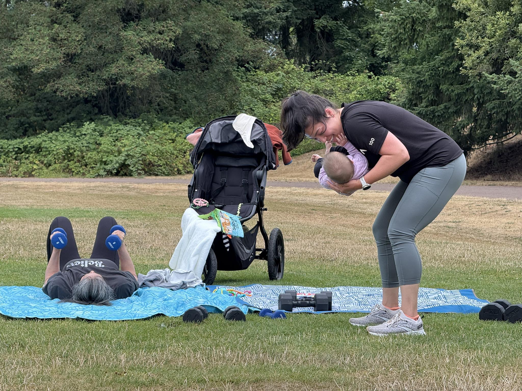 Mom holding baby while another member exercises at outdoor class