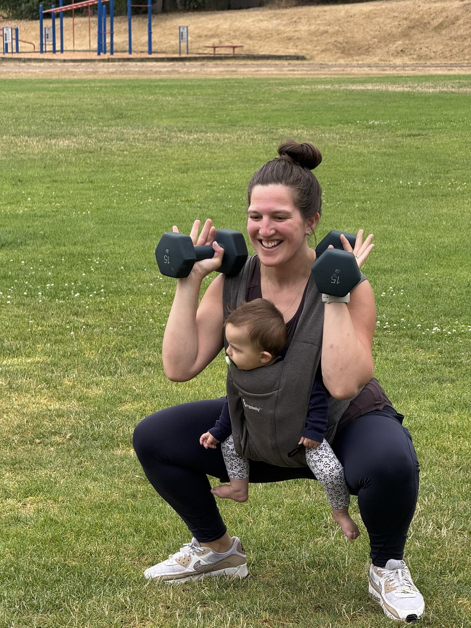 Mom doing squats with dumbbells while wearing baby in carrier
